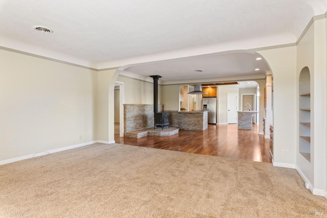 unfurnished living room with built in features, carpet, a wood stove, and ornamental molding