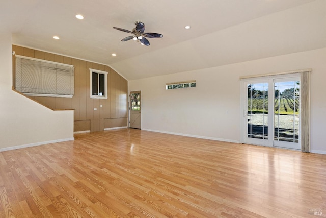 unfurnished living room with light hardwood / wood-style floors, vaulted ceiling, ceiling fan, and wooden walls