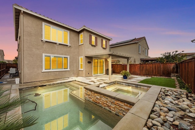 back house at dusk featuring a swimming pool with hot tub