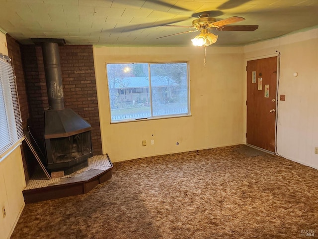 unfurnished living room featuring carpet, a wood stove, and ceiling fan