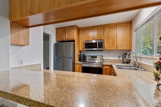 kitchen featuring light stone counters, sink, kitchen peninsula, and appliances with stainless steel finishes