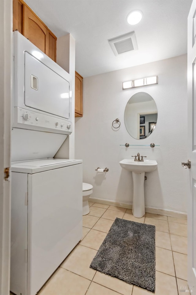 bathroom with tile patterned flooring, stacked washer / drying machine, and toilet