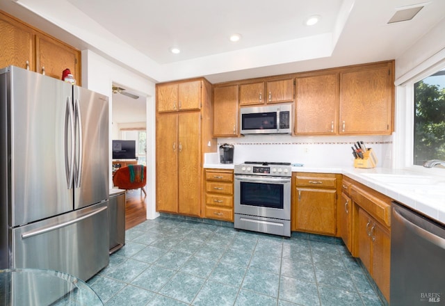 kitchen with appliances with stainless steel finishes, a tray ceiling, tasteful backsplash, and sink