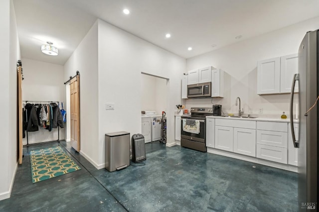 kitchen with washer and clothes dryer, stainless steel appliances, a barn door, white cabinetry, and a sink