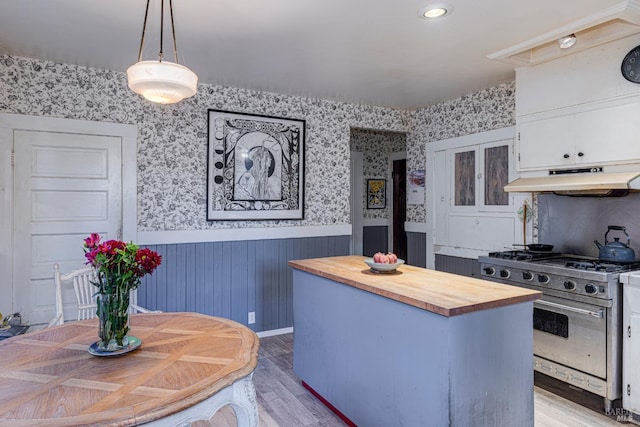 kitchen featuring hanging light fixtures, a center island, wood counters, stainless steel gas range oven, and white cabinets