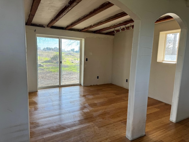 unfurnished room with beam ceiling, a wealth of natural light, and light wood-type flooring