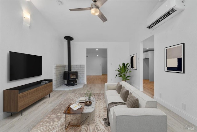 living room with a wall mounted air conditioner, ceiling fan, a wood stove, and light hardwood / wood-style flooring