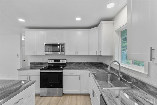 kitchen with dark stone counters, white cabinets, sink, light wood-type flooring, and stainless steel appliances