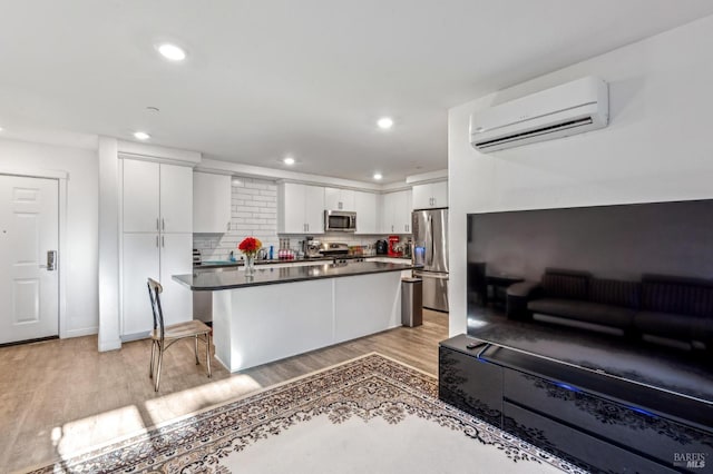 kitchen with a wall mounted air conditioner, a kitchen breakfast bar, light wood-type flooring, stainless steel appliances, and white cabinets