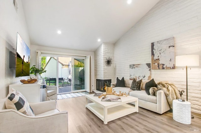 living area with a large fireplace, wood finished floors, and high vaulted ceiling