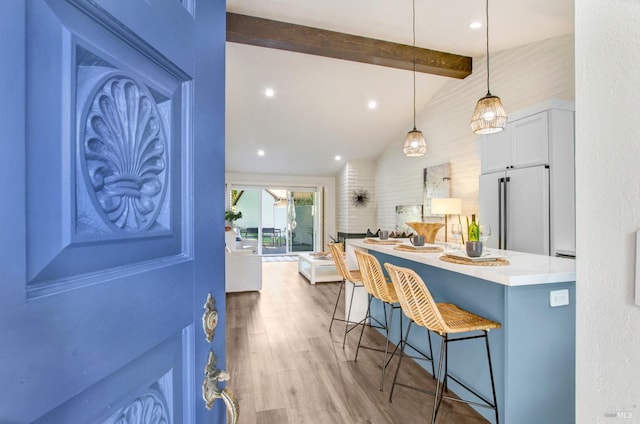 kitchen with wood finished floors, vaulted ceiling with beams, high end fridge, a kitchen bar, and decorative light fixtures