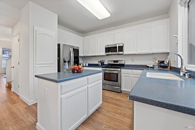 kitchen with a center island, white cabinets, sink, light wood-type flooring, and appliances with stainless steel finishes