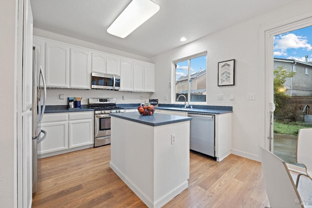 kitchen featuring appliances with stainless steel finishes, light wood-type flooring, sink, white cabinets, and a center island