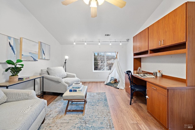 office area featuring ceiling fan, rail lighting, light hardwood / wood-style flooring, vaulted ceiling, and built in desk