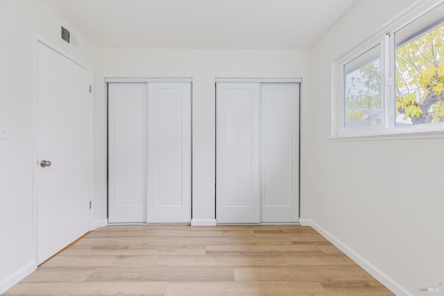 unfurnished bedroom with light hardwood / wood-style floors and two closets