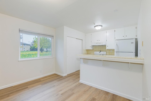 kitchen featuring white cabinets, white refrigerator, light hardwood / wood-style floors, a kitchen bar, and kitchen peninsula