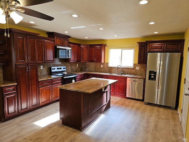 kitchen with light stone countertops, light wood-type flooring, stainless steel appliances, sink, and a kitchen island