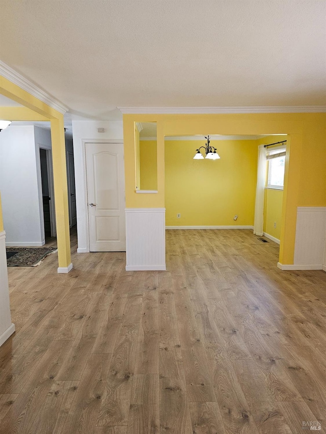 unfurnished living room featuring a textured ceiling, light wood-type flooring, an inviting chandelier, and crown molding