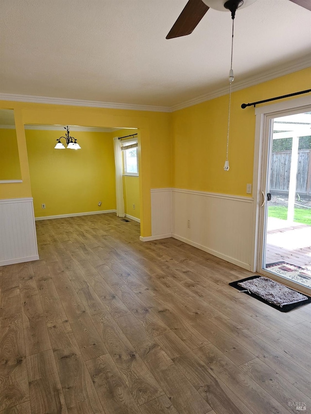 empty room featuring a healthy amount of sunlight, ceiling fan, wood-type flooring, and ornamental molding