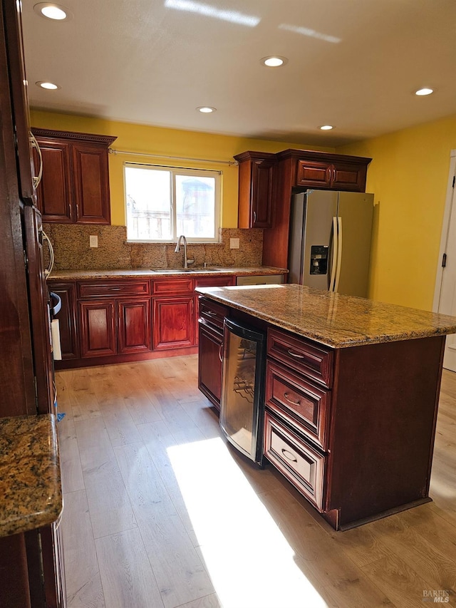 kitchen with sink, stainless steel refrigerator with ice dispenser, backsplash, a kitchen island, and light wood-type flooring