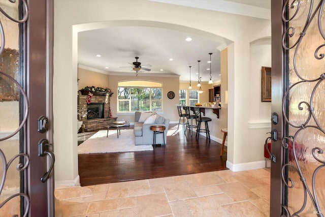 living room with a fireplace, light wood-type flooring, ceiling fan, and crown molding