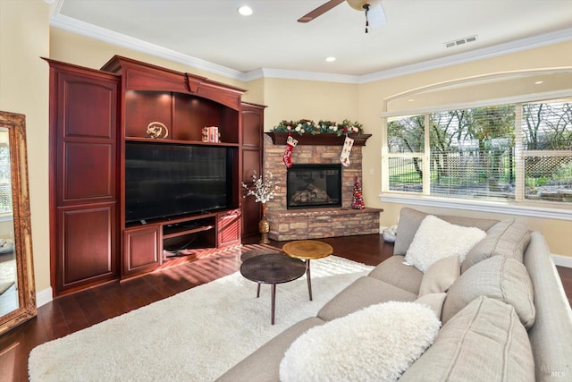 living room featuring crown molding, ceiling fan, dark wood-type flooring, and a stone fireplace