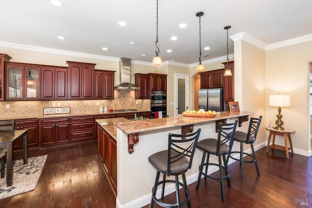 kitchen with appliances with stainless steel finishes, wall chimney exhaust hood, a breakfast bar, dark wood-type flooring, and decorative light fixtures