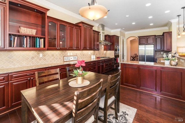 kitchen featuring light stone countertops, appliances with stainless steel finishes, dark hardwood / wood-style flooring, wall chimney range hood, and decorative light fixtures