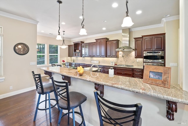 kitchen with appliances with stainless steel finishes, a breakfast bar, wall chimney range hood, pendant lighting, and dark hardwood / wood-style floors