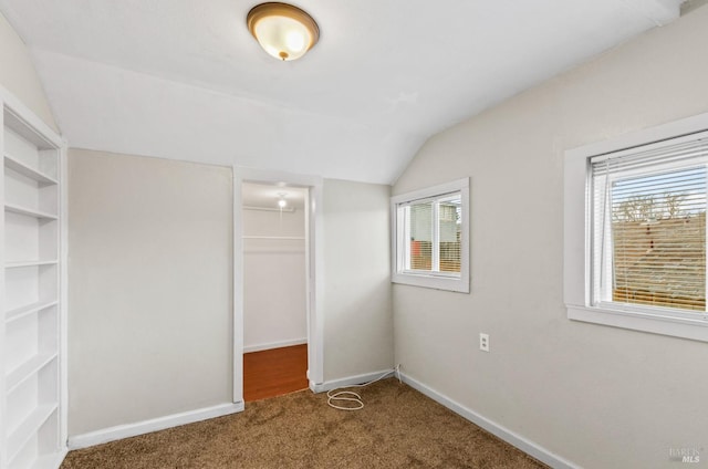 unfurnished bedroom with a spacious closet, vaulted ceiling, a closet, and carpet