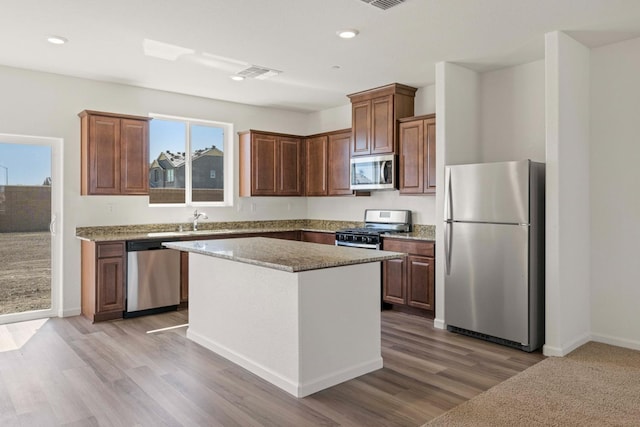 kitchen with light stone countertops, sink, a center island, light hardwood / wood-style floors, and appliances with stainless steel finishes