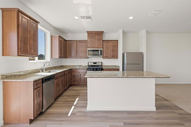 kitchen featuring sink, a center island, light stone countertops, and appliances with stainless steel finishes