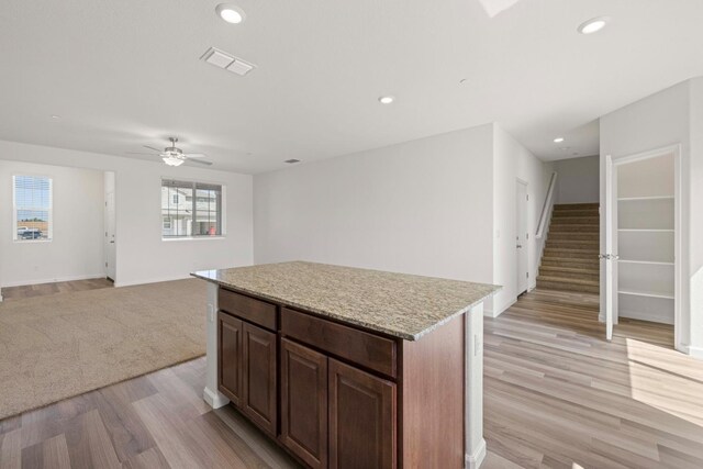 kitchen with light stone counters, dark brown cabinetry, ceiling fan, a center island, and light hardwood / wood-style floors