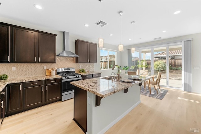 kitchen with pendant lighting, sink, a breakfast bar area, wall chimney exhaust hood, and gas range