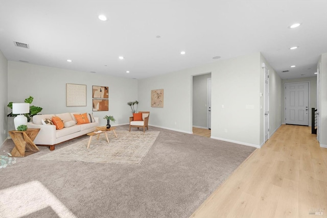 living area featuring visible vents, light carpet, light wood-style flooring, recessed lighting, and baseboards