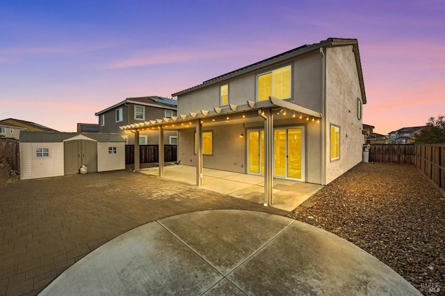 back of house at dusk with a patio, an outbuilding, a shed, a fenced backyard, and stucco siding