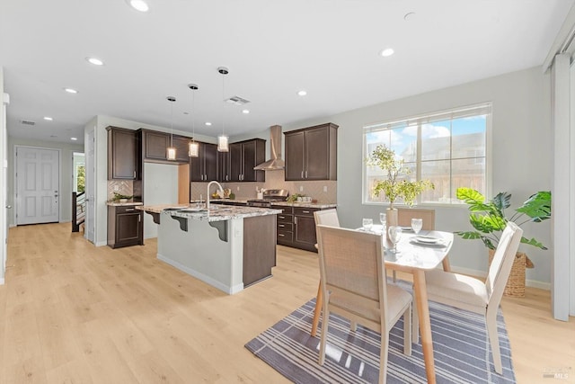 kitchen with stove, wall chimney range hood, dark brown cabinets, and light wood-style floors