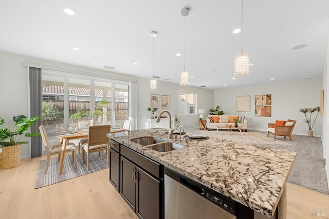 kitchen with a sink, decorative light fixtures, stainless steel dishwasher, open floor plan, and light stone countertops