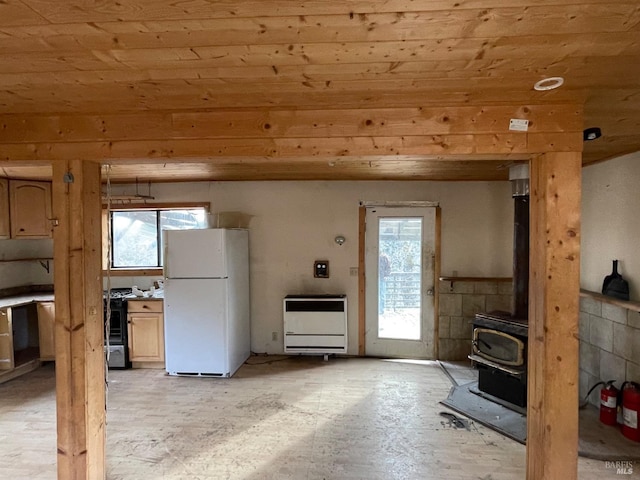 kitchen featuring light brown cabinetry, white refrigerator, a wood stove, and wooden ceiling