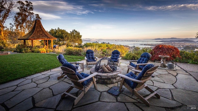 patio terrace at dusk with a gazebo, a yard, a water view, and an outdoor fire pit