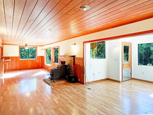 living room with light hardwood / wood-style floors, a wood stove, wood walls, and wood ceiling