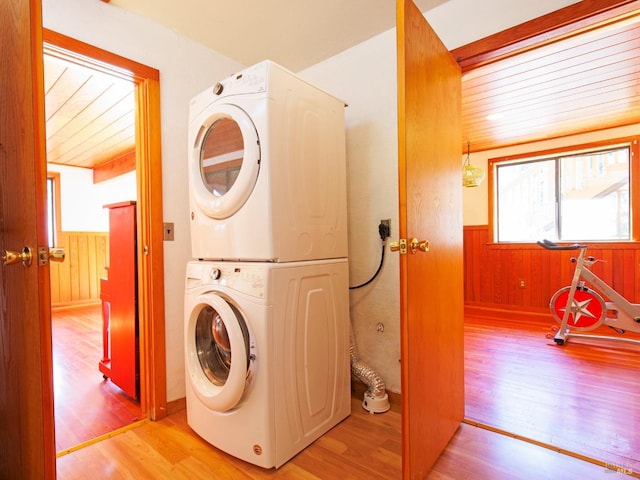 clothes washing area featuring wooden ceiling, light hardwood / wood-style flooring, stacked washer and clothes dryer, and wood walls