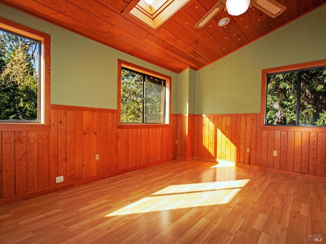 empty room featuring wood walls, lofted ceiling with skylight, wooden ceiling, ceiling fan, and light hardwood / wood-style floors