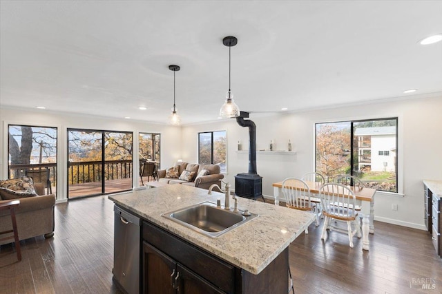 kitchen with a wood stove, sink, stainless steel dishwasher, an island with sink, and pendant lighting