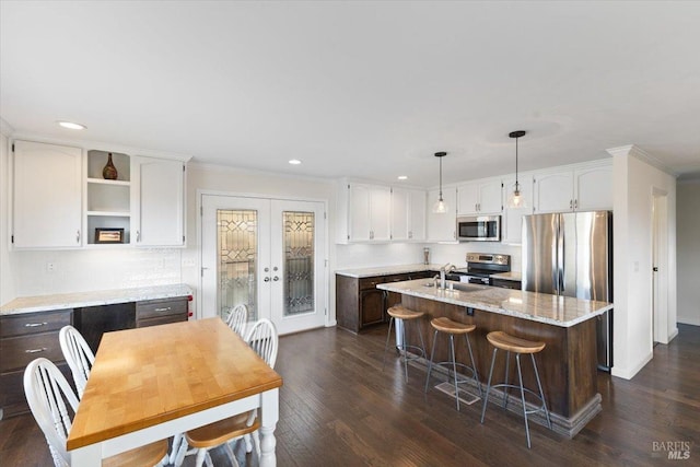 kitchen with light stone countertops, white cabinetry, an island with sink, and stainless steel appliances