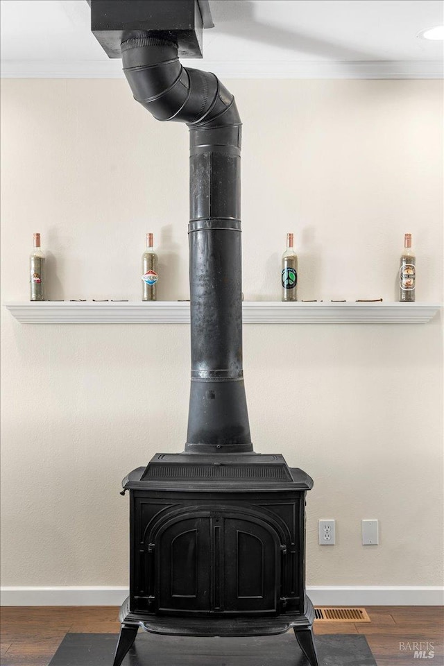 interior details featuring wood-type flooring, a wood stove, and crown molding