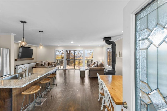 kitchen with a breakfast bar, sink, pendant lighting, a wood stove, and stainless steel refrigerator