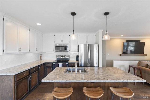 kitchen with appliances with stainless steel finishes, a center island with sink, light stone counters, and white cabinetry