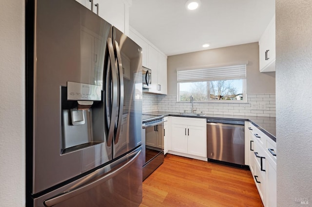 kitchen featuring white cabinetry, sink, stainless steel appliances, light hardwood / wood-style flooring, and backsplash