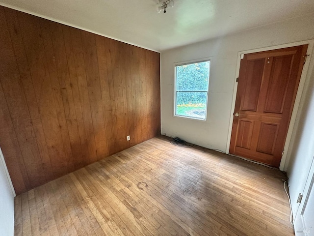 unfurnished room with light wood-type flooring and wood walls